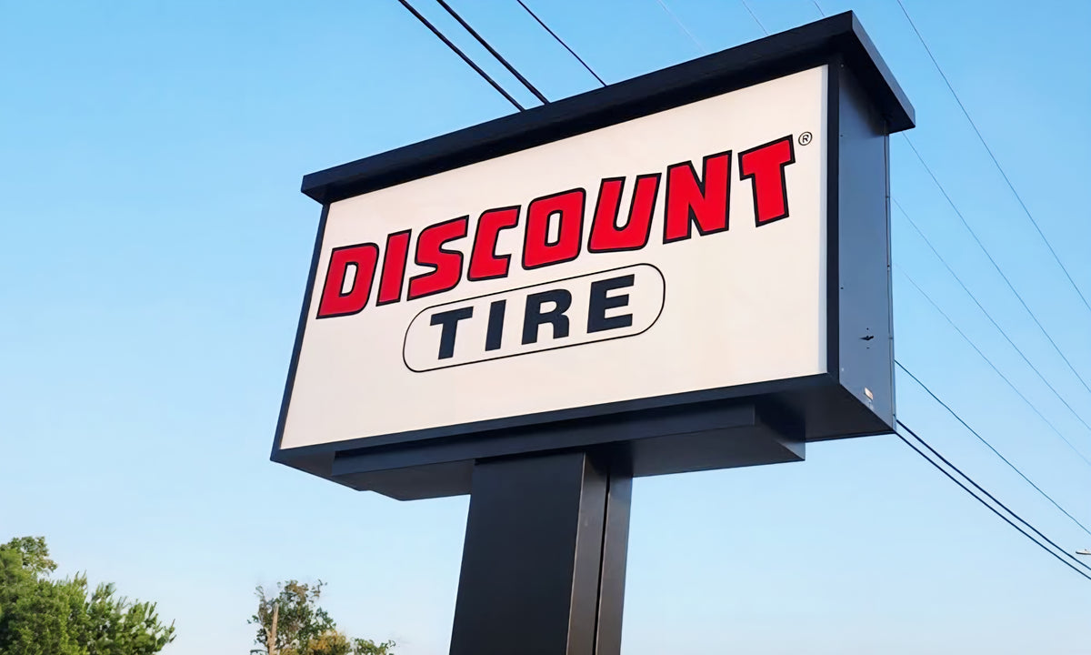 A large roadside Discount Tire sign with bold red and black lettering against a clear blue sky, with power lines visible in the background.